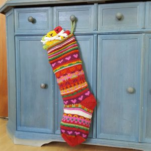 Hand knit Christmas stocking with colorful stripes and heart motifs, artisan made