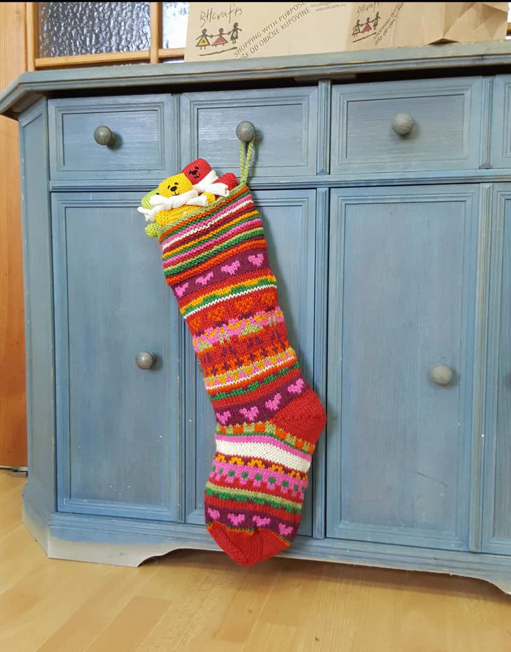 Hand knit Christmas stocking with colorful stripes and heart motifs, artisan made