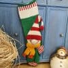 Green and red hand-knit Christmas stocking with elf appliqué hanging on a blue cabinet
