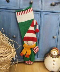 Green and red hand-knit Christmas stocking with elf appliqué hanging on a blue cabinet