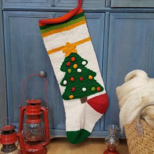 Hand-knitted Christmas stocking with green tree design, colorful ornaments, and striped cuff, hanging.