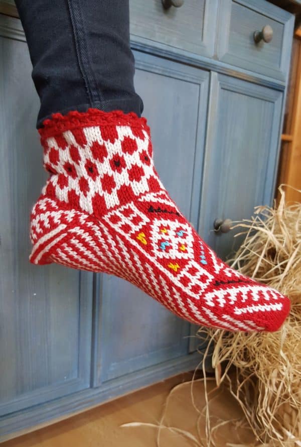 Hand knit wool slipper socks with a red and white Bosnian pattern on a person’s feet.