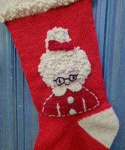 Close-up of hand-knitted Mrs. Claus Christmas stocking showing detailed face motif with glasses, curly hair, and festive hat.