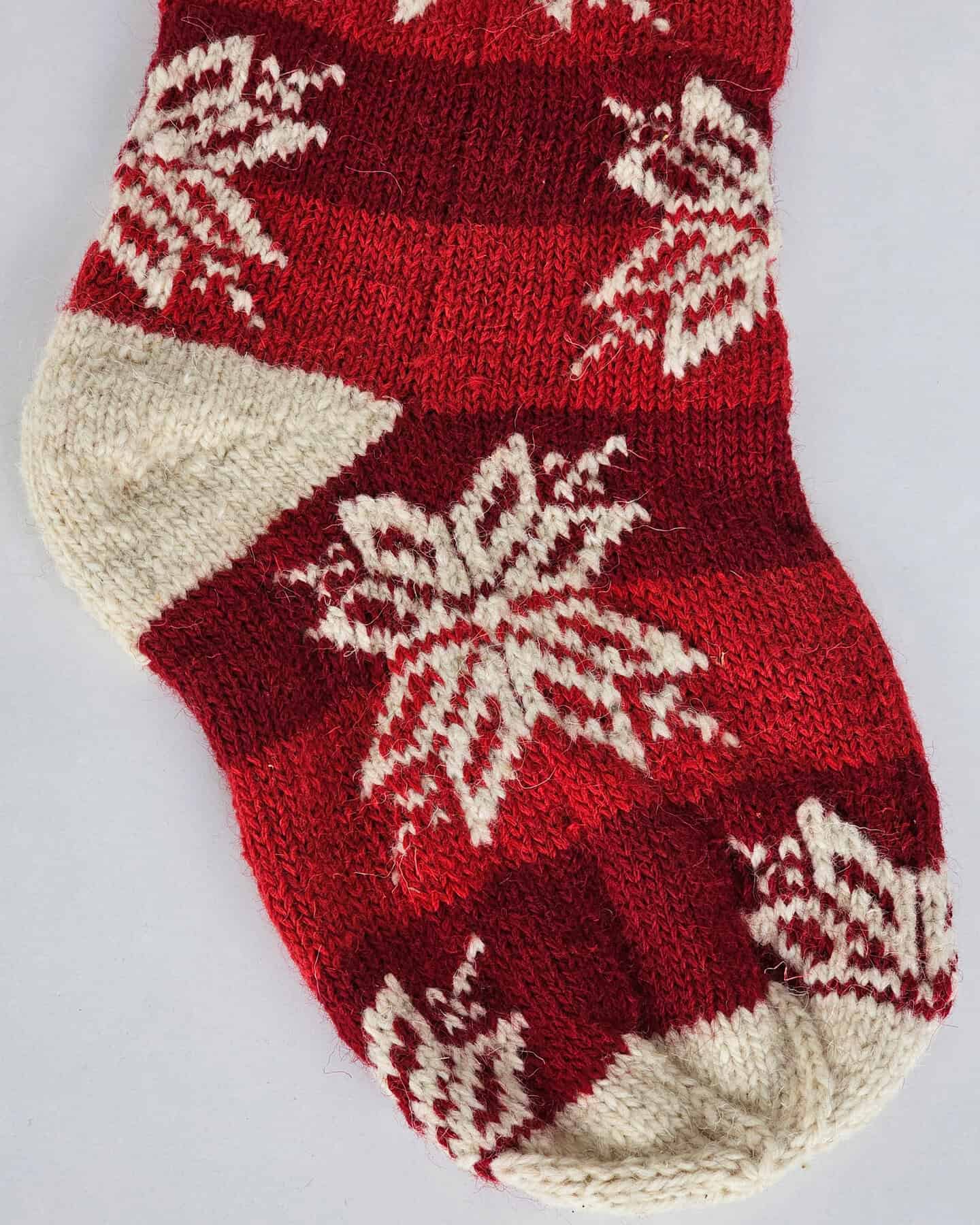 Close-up of red and white hand-knitted Christmas stocking with snowflake pattern.