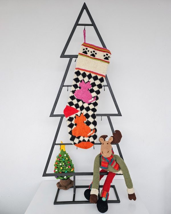 Checkerboard Christmas stocking featuring stylized cats in pink and orange on cream and black background.