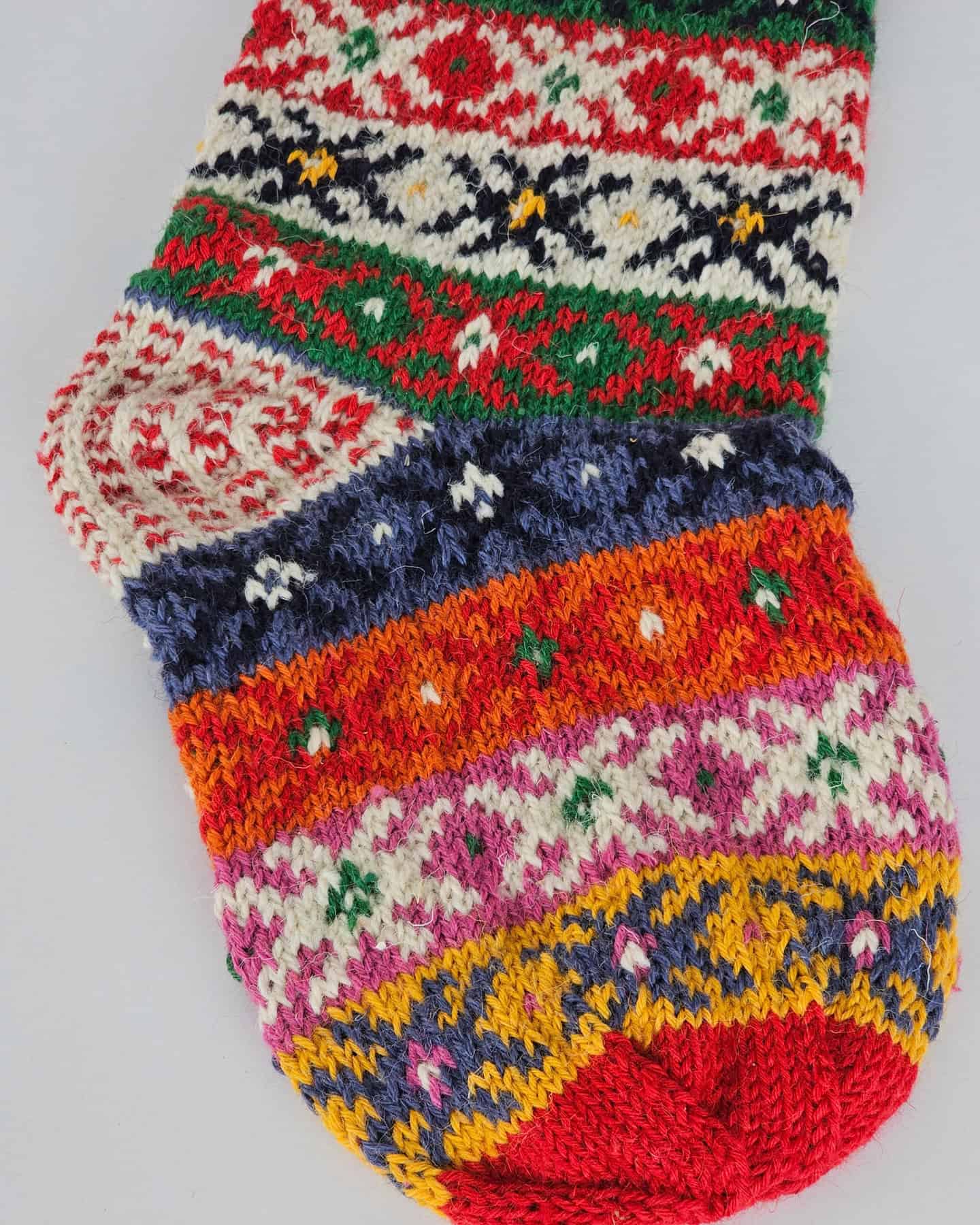 Handmade Christmas stocking featuring vibrant stripes and folk-inspired knit motifs.