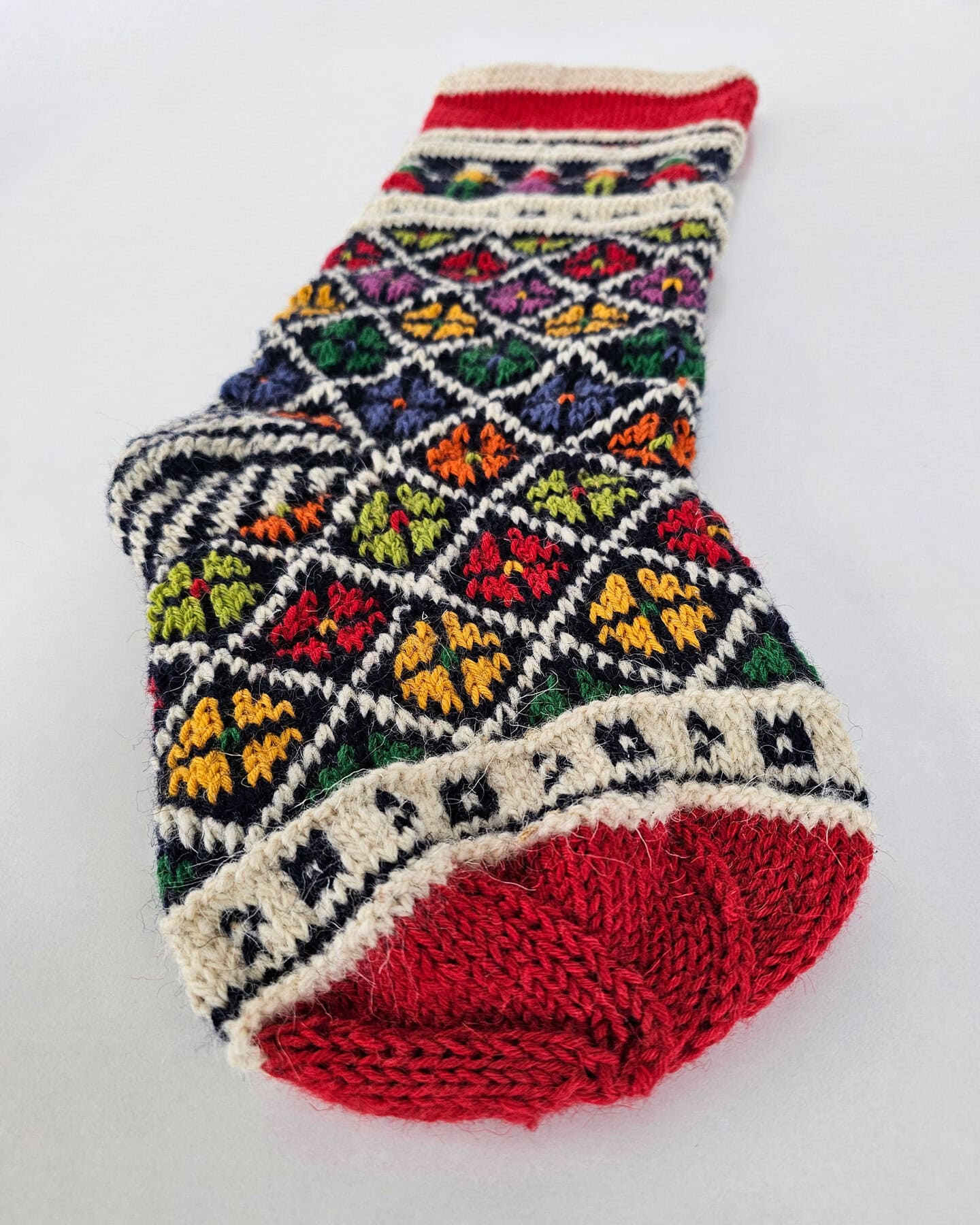 Beautiful hand-knitted Christmas stocking with festive folk art motifs and multicolor design, personalized for a Custom Name.