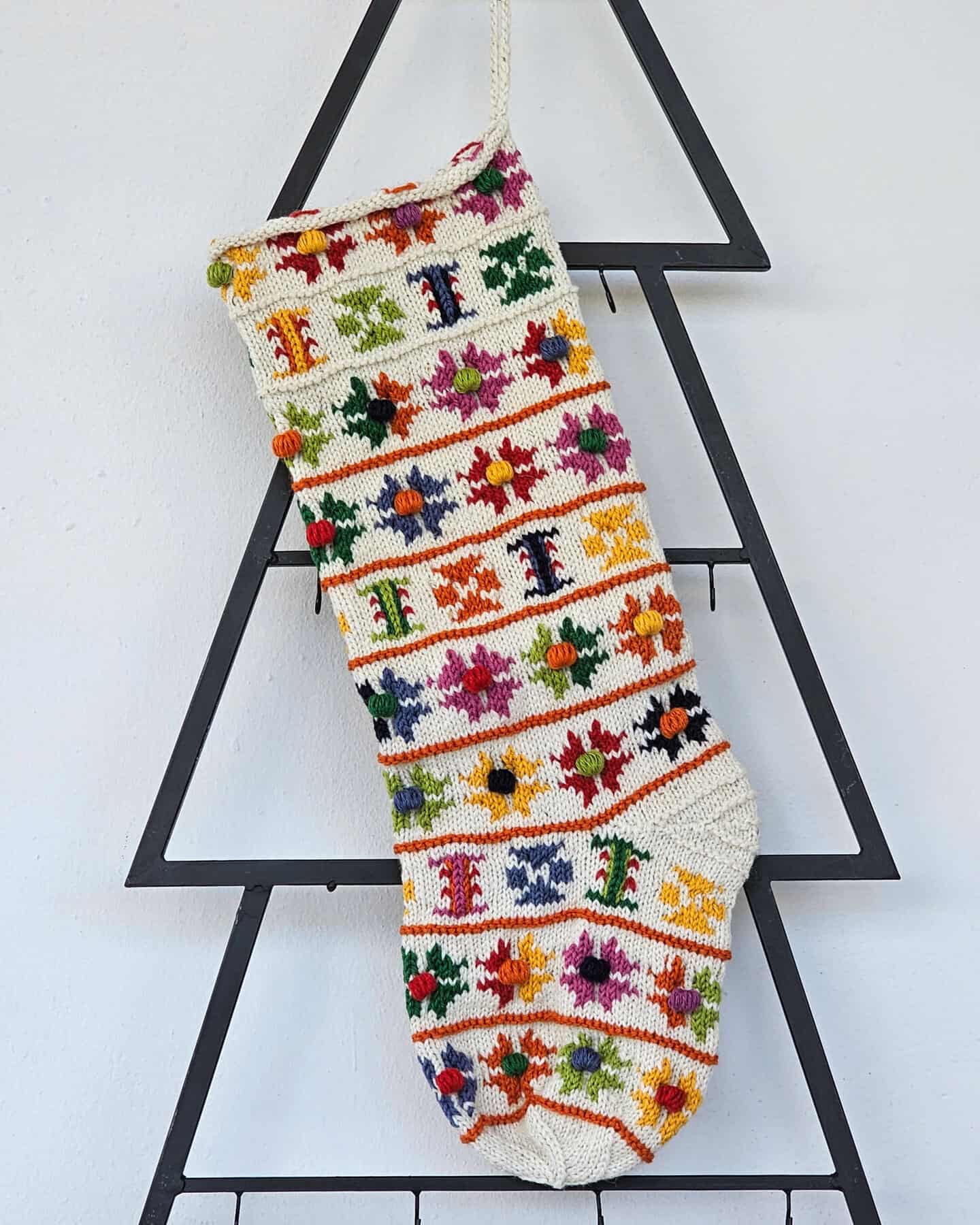 Hand-knit Christmas stocking with colorful floral patterns and pom-poms