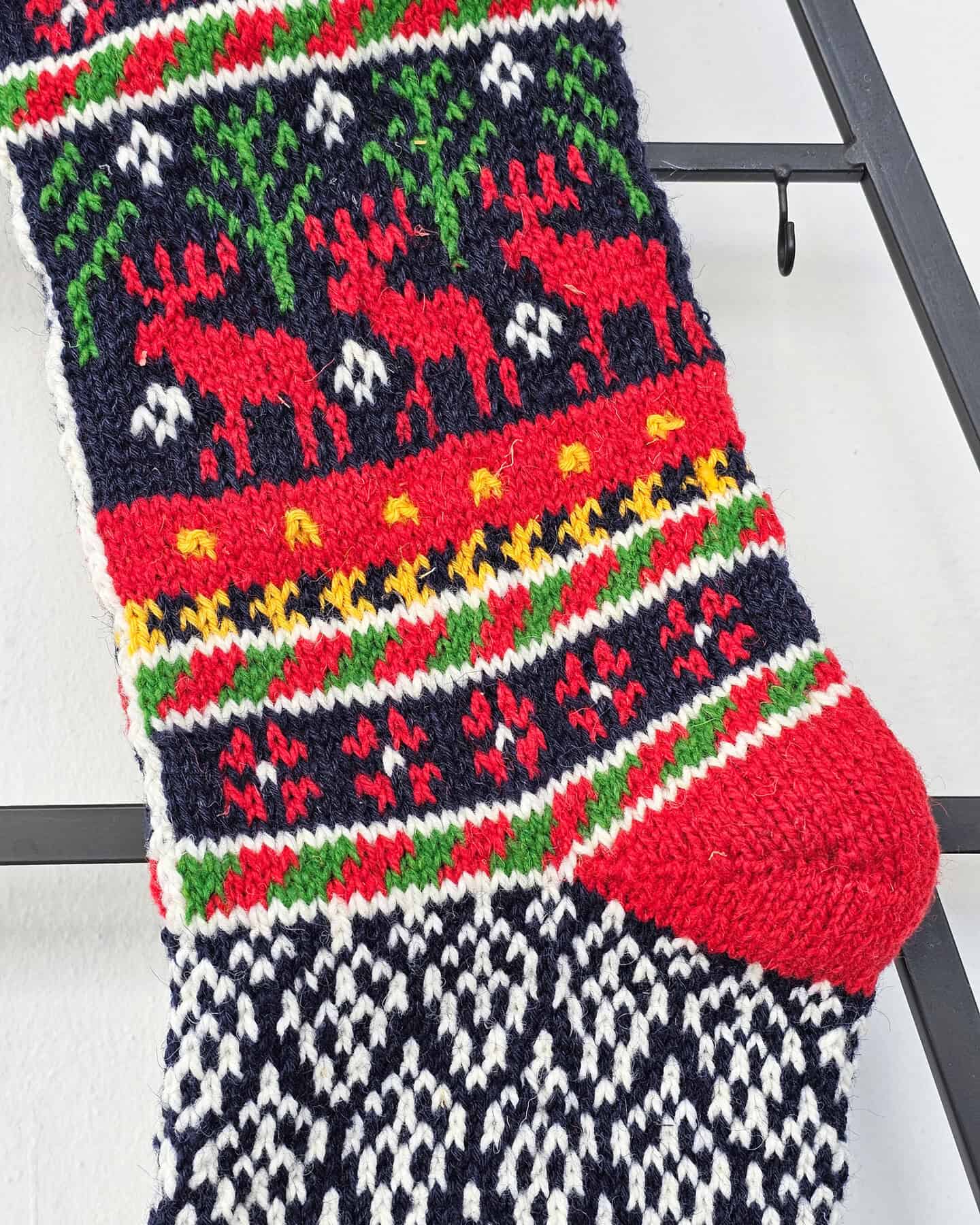 Handmade Christmas stocking held in hand showing detailed reindeer design and traditional red and white patterns.