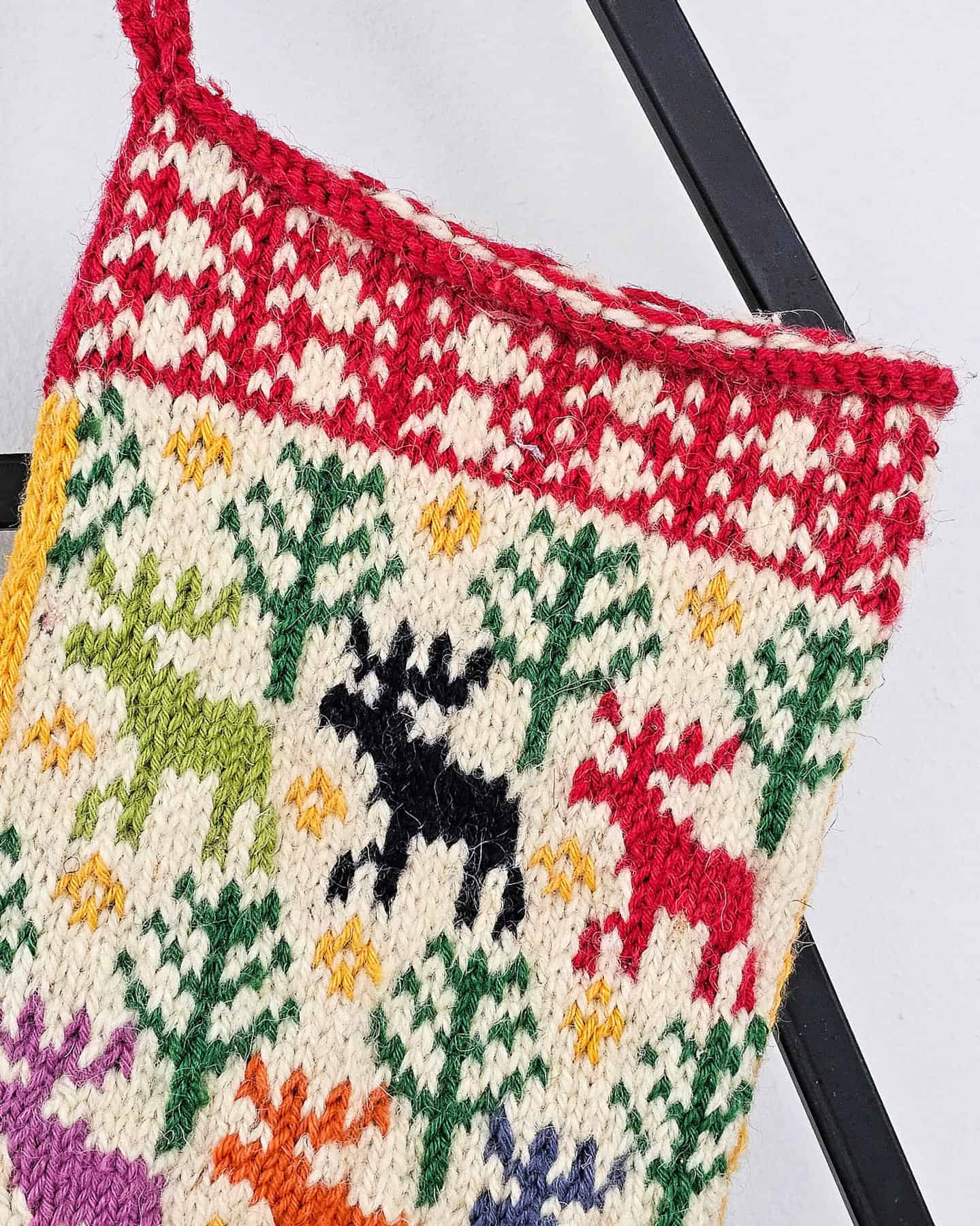 Bright red knitted Christmas stocking with green trees, white snowflakes, and yellow bells in a festive pattern.