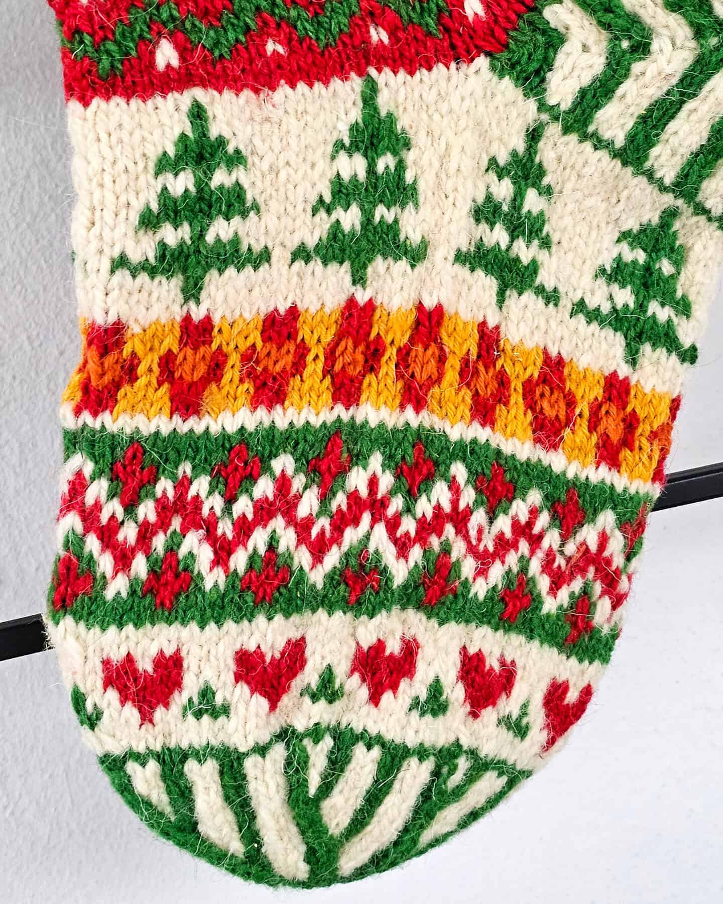 Christmas stocking held in hand showing knitted details of reindeer, Santa, and tree patterns.