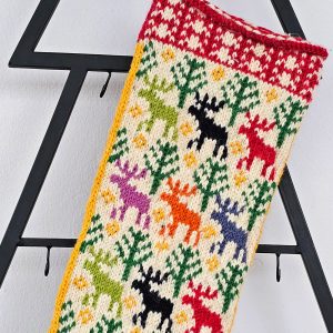Close-up of a colorful knitted Christmas stocking with snowmen, trees, and bells in red, white, green, and blue yarn.