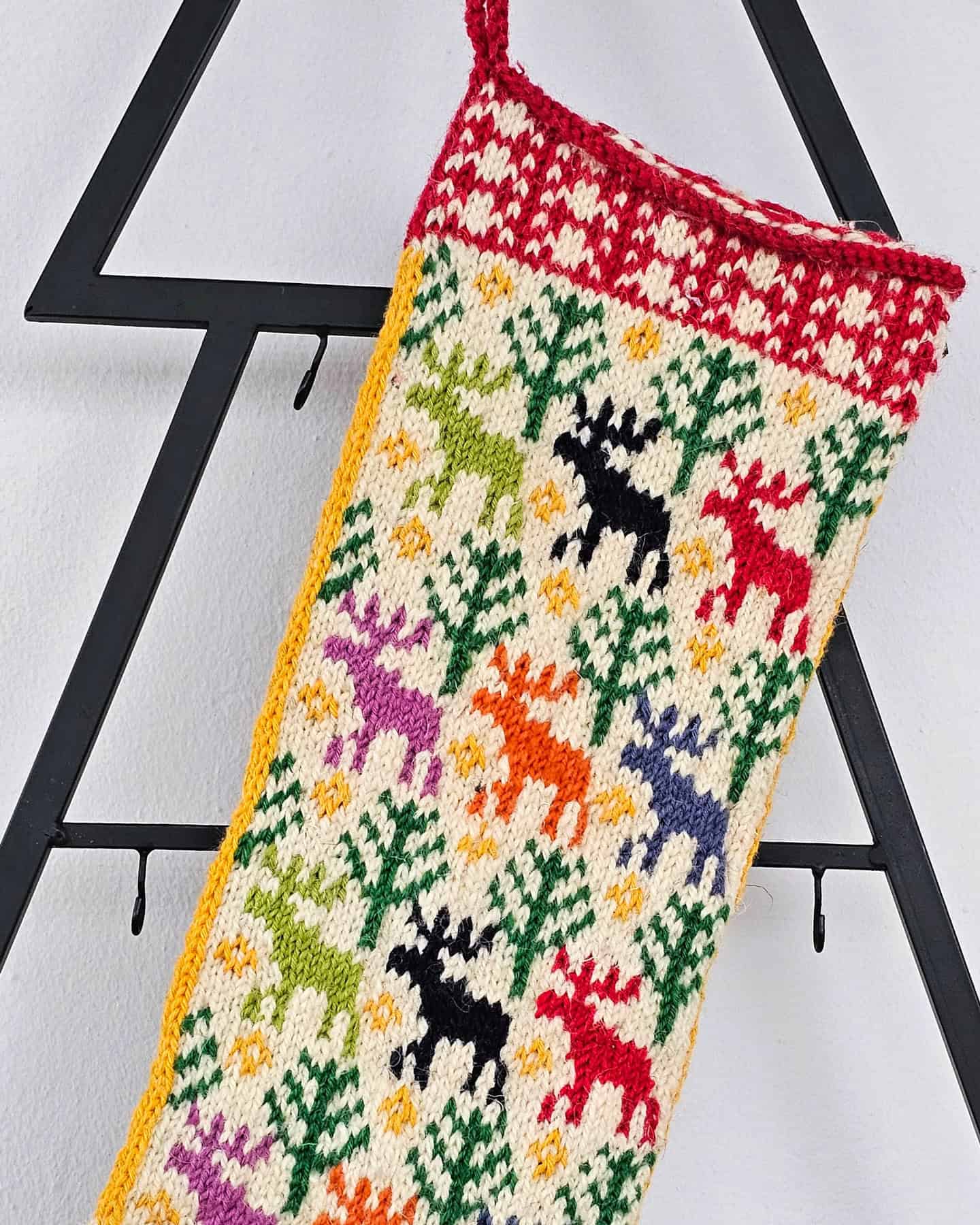 Close-up of a colorful knitted Christmas stocking with snowmen, trees, and bells in red, white, green, and blue yarn.