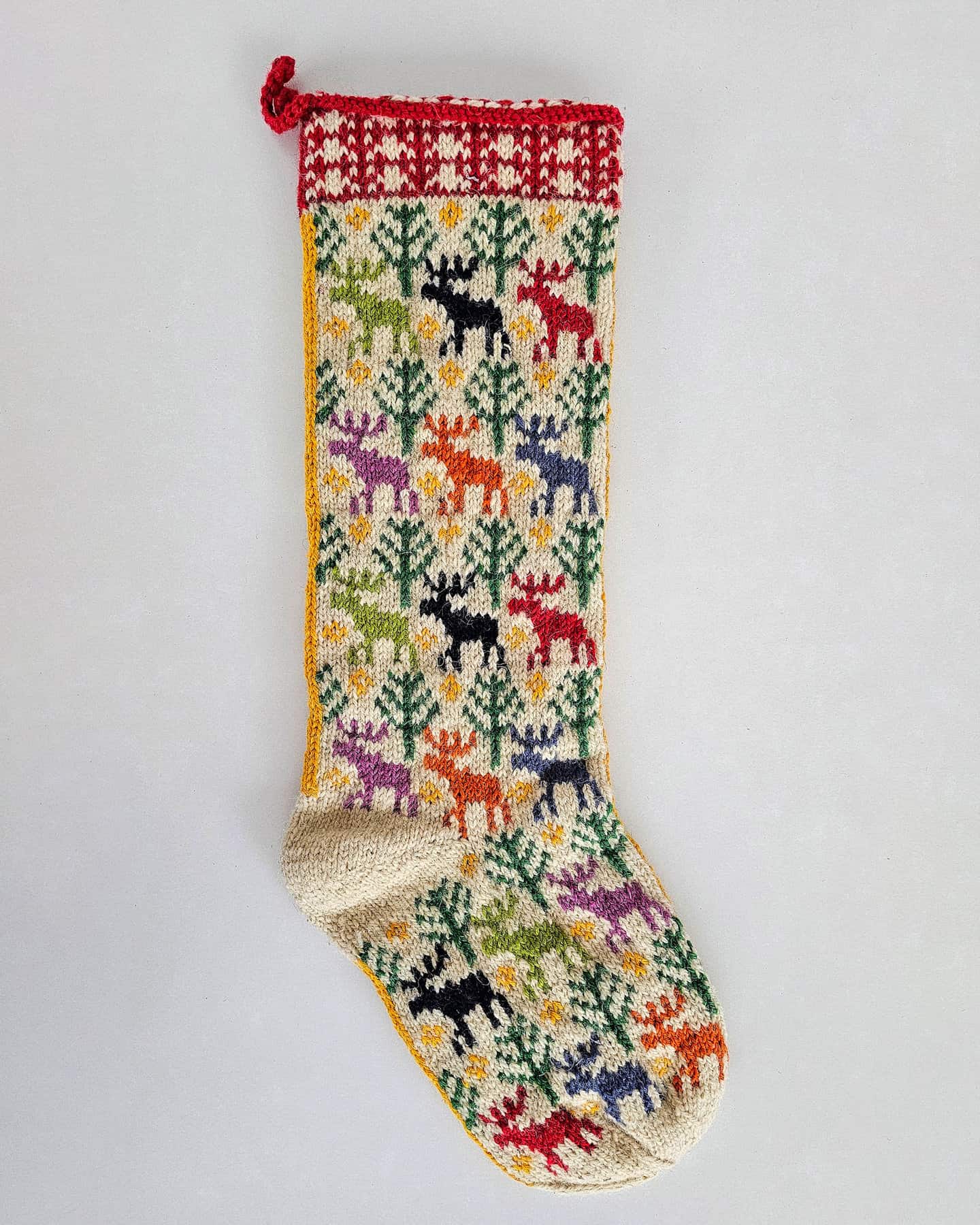 A colorful knitted Christmas stocking featuring festive patterns of snowmen, trees, and bells in red, green, white, and blue yarn.