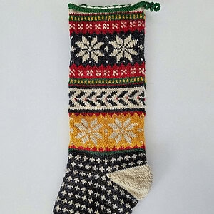 Hand-knitted Christmas stocking featuring Nordic-inspired snowflake patterns, chevron stripes, and fair isle motifs in festive tones.