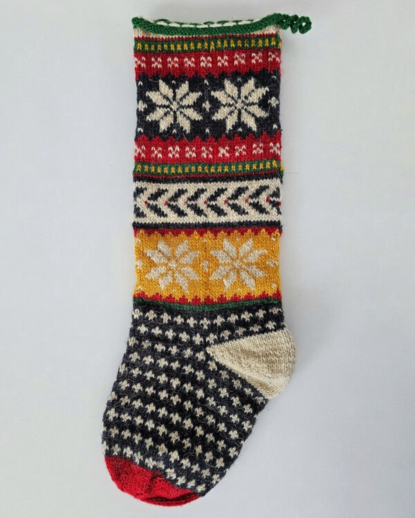 Hand-knitted Christmas stocking featuring Nordic-inspired snowflake patterns, chevron stripes, and fair isle motifs in festive tones.