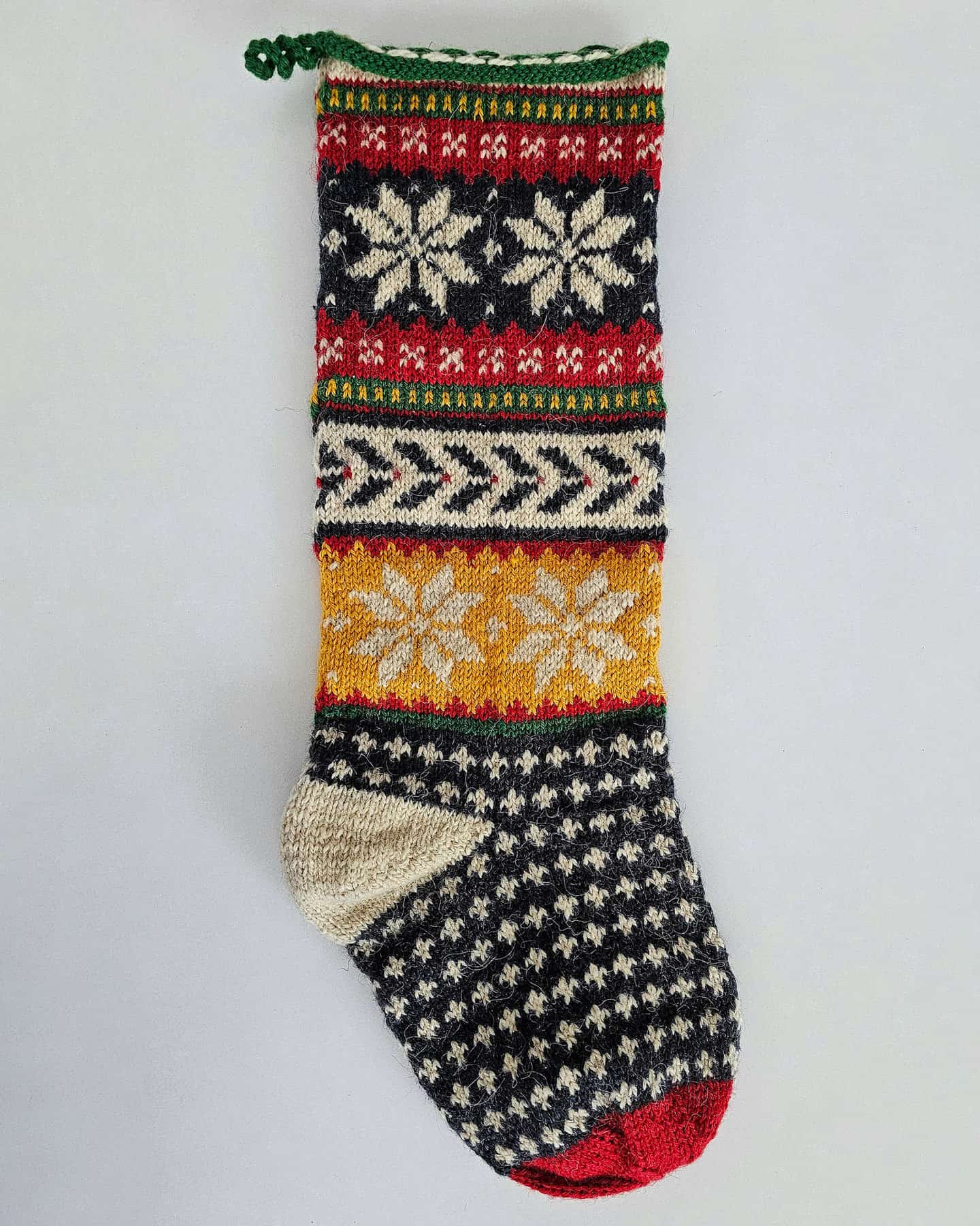 Hand-knitted Christmas stocking featuring Nordic-inspired snowflake patterns, chevron stripes, and fair isle motifs in festive tones.