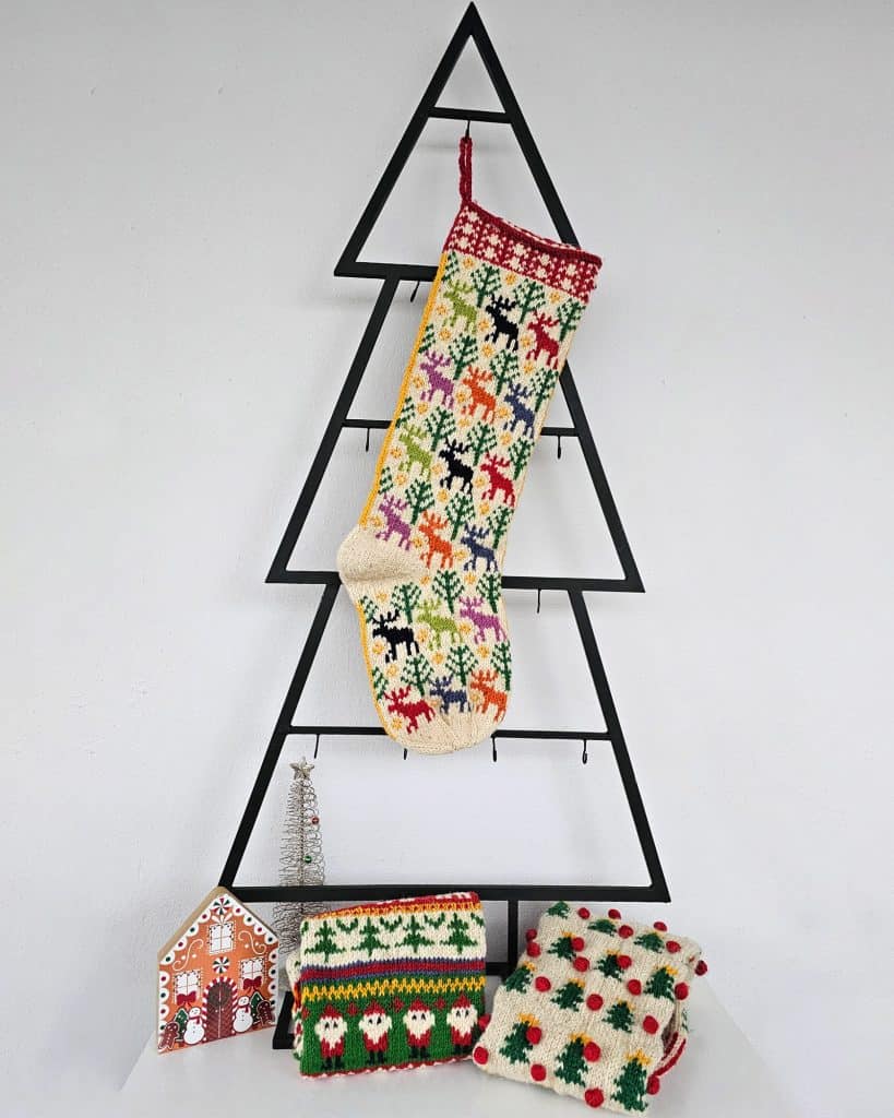 Colorful hand-knitted Christmas stocking featuring festive patterns of reindeer and trees in red, green, white, and beige.