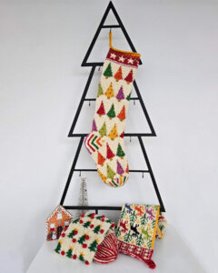 Hand‑knitted Christmas stocking in red, green and cream with traditional Bosnian geometric motifs hanging against a light grey background.