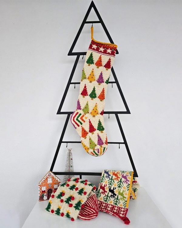 Hand‑knitted Christmas stocking in red, green and cream with traditional Bosnian geometric motifs hanging against a light grey background.