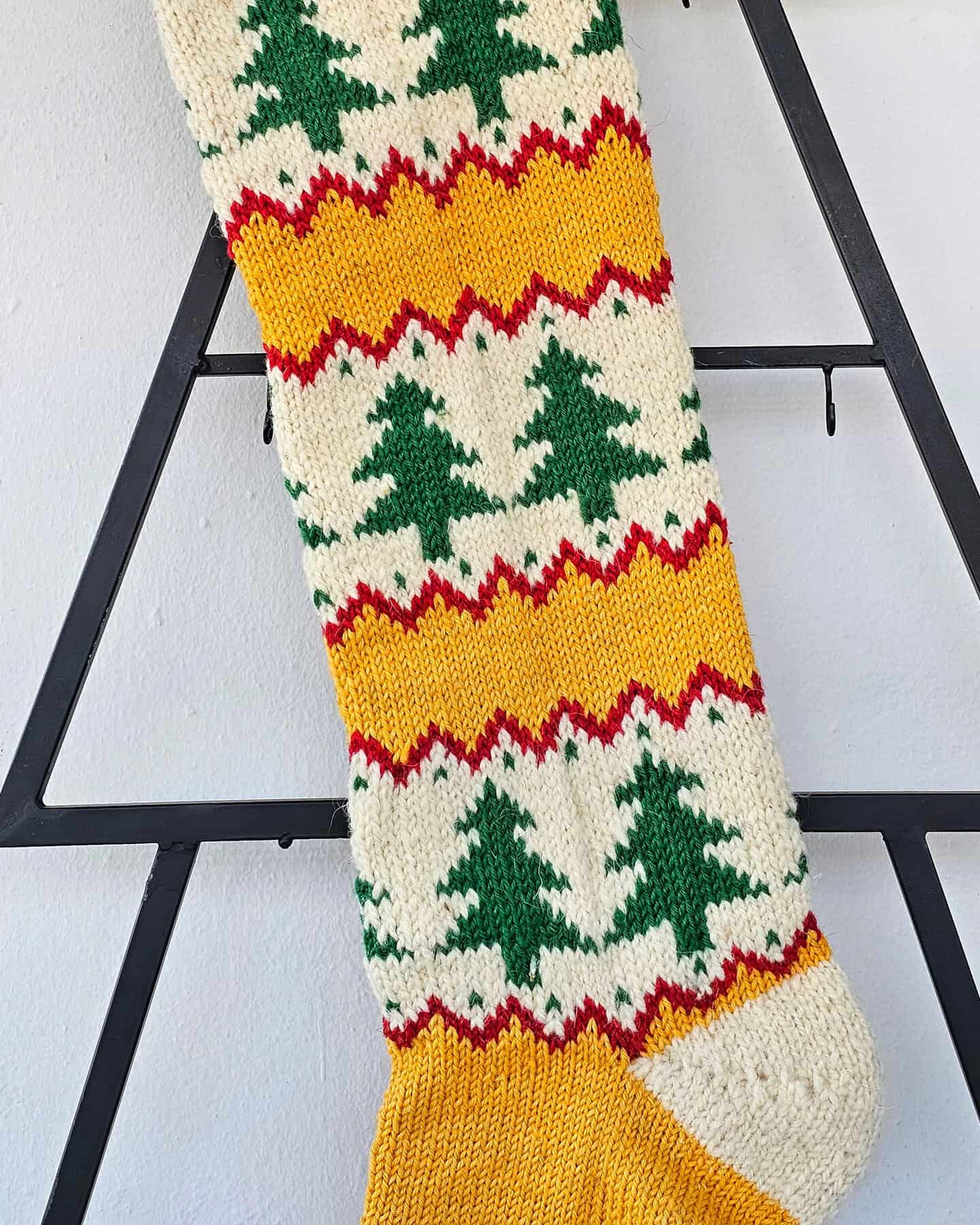 Hand‑knitted Christmas stocking with chevron‑tree pattern in red, cream, and green
