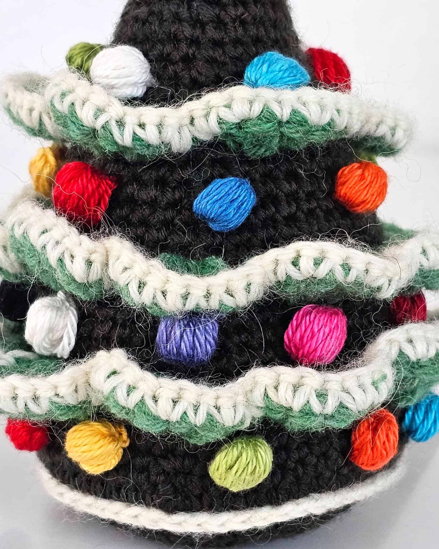 Side view of a handmade fair trade crocheted Christmas tree ornament showing layered green branches and snow-like white edges.