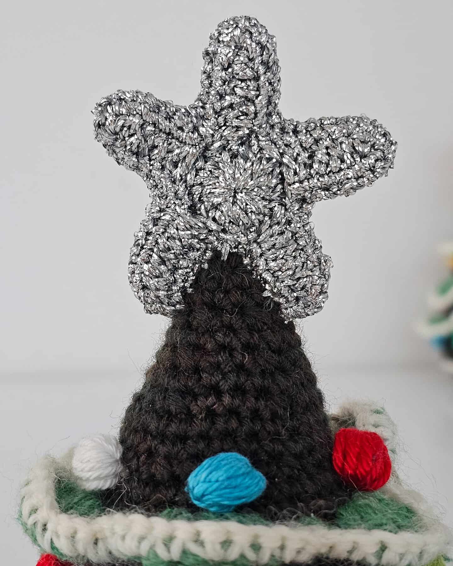 Top-down view of crochet Christmas tree christmas décor highlighting the silver star topper and colorful bobble decorations.