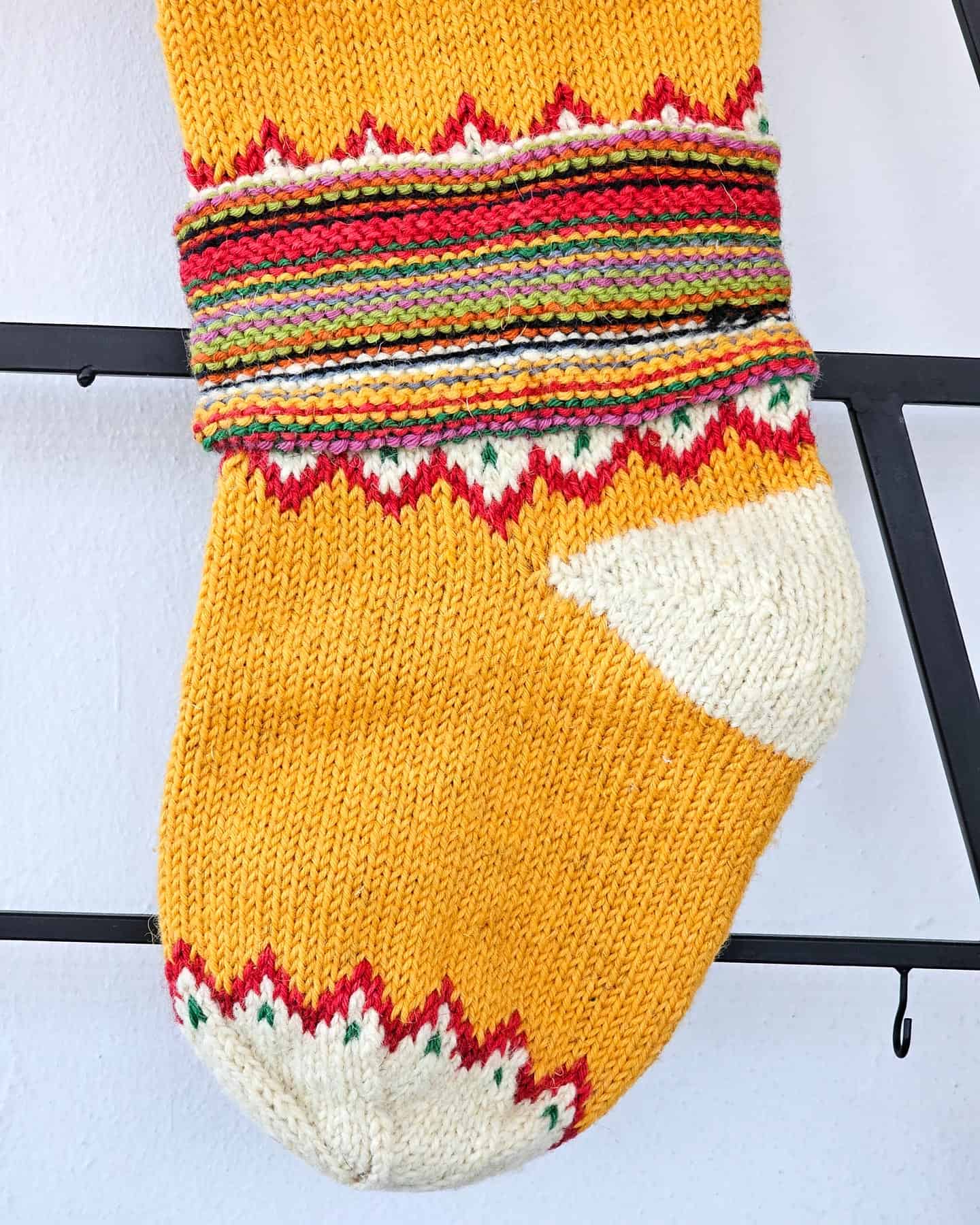Detailed knitting pattern of sustainable handmade Christmas stocking in red, yellow, green and purple yarns.