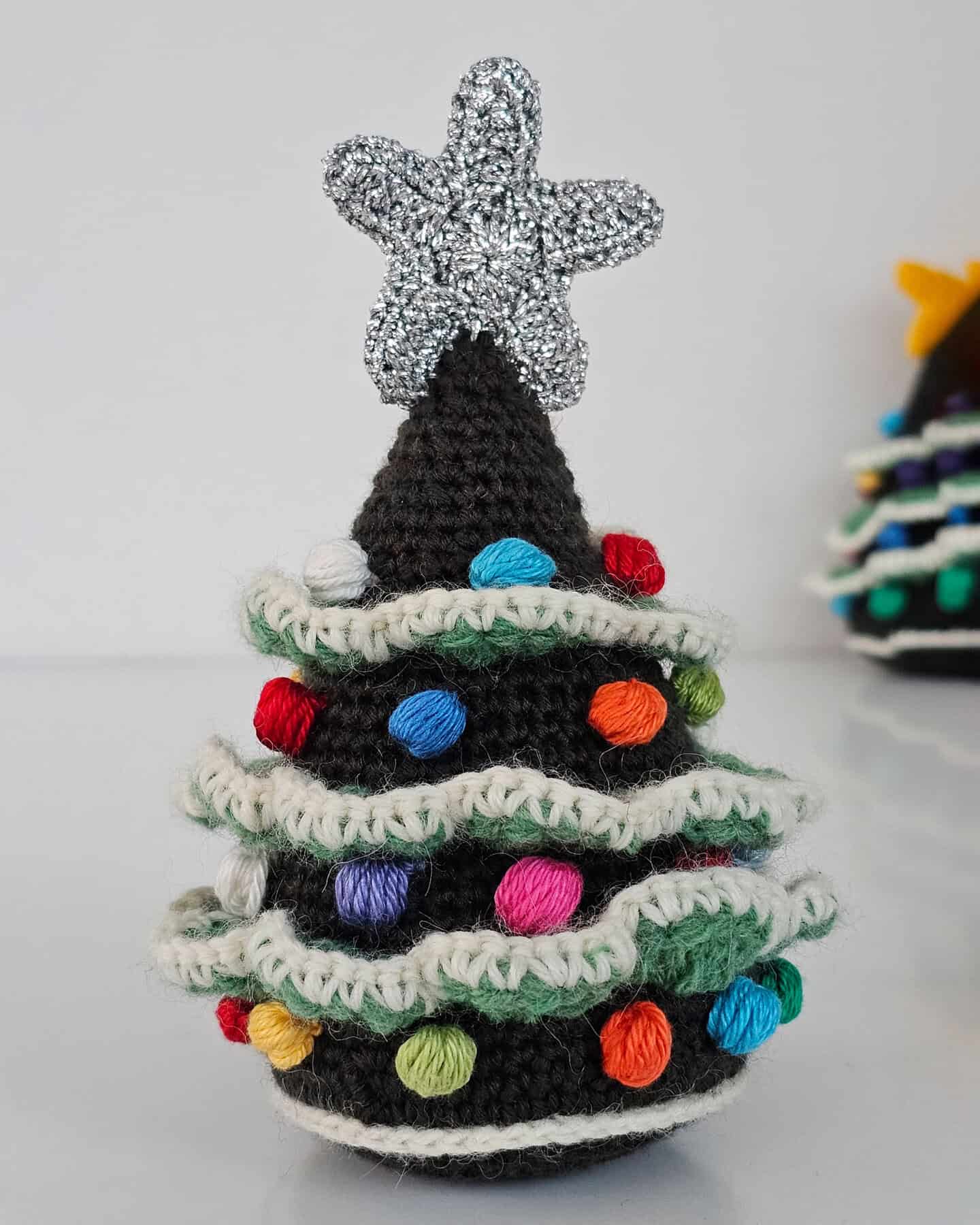 Handmade crocheted eco-friendly Christmas tree ornament with layered green branches, white snow-like edges, multicolor bobbles, and silver star topper.