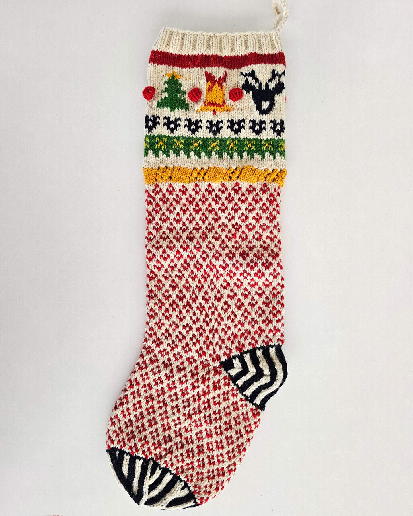 Hand-knitted Christmas stocking with reindeer, tree, and bell design