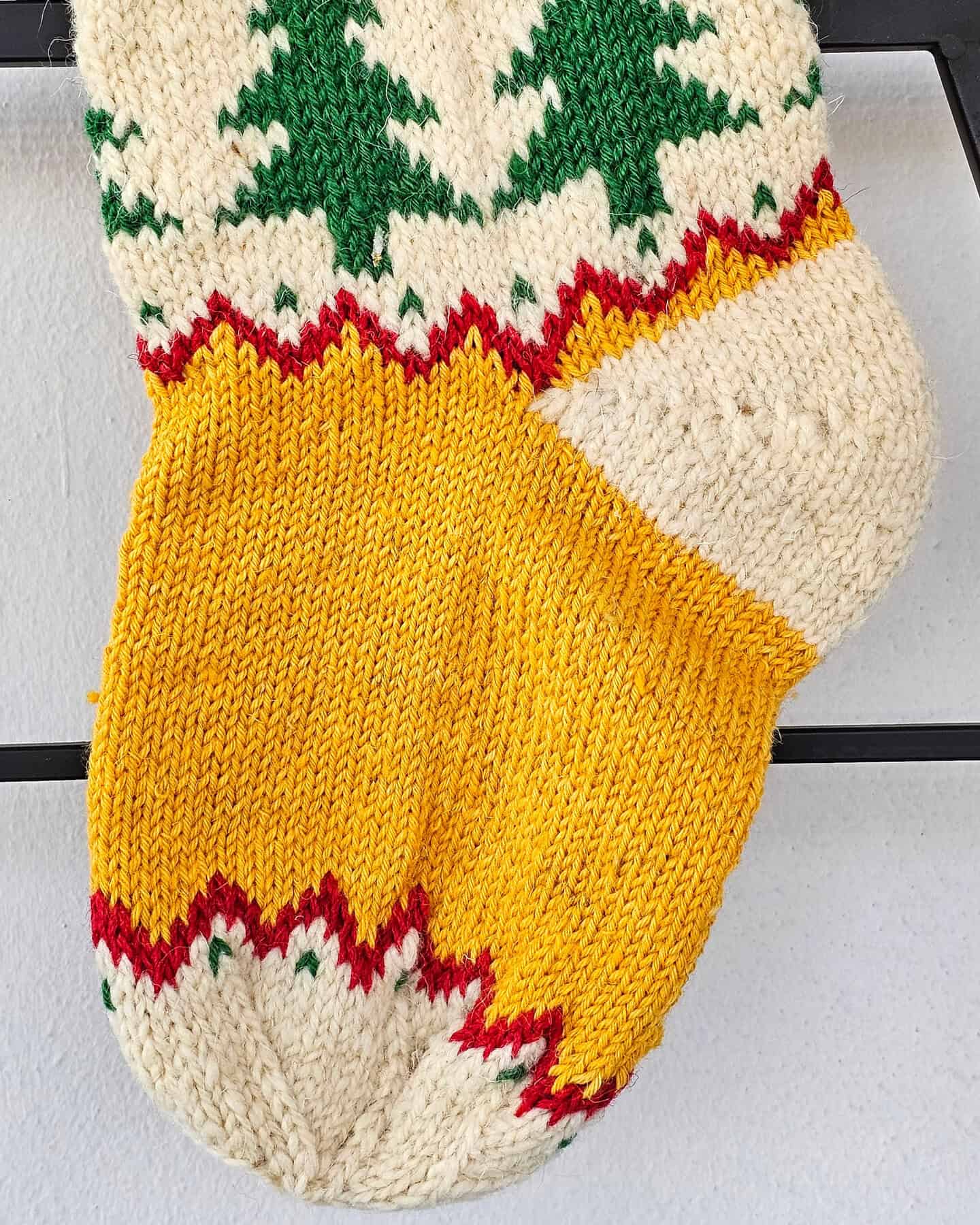 Hand‑knitted Christmas stocking with chevron‑tree pattern in red, cream, and green