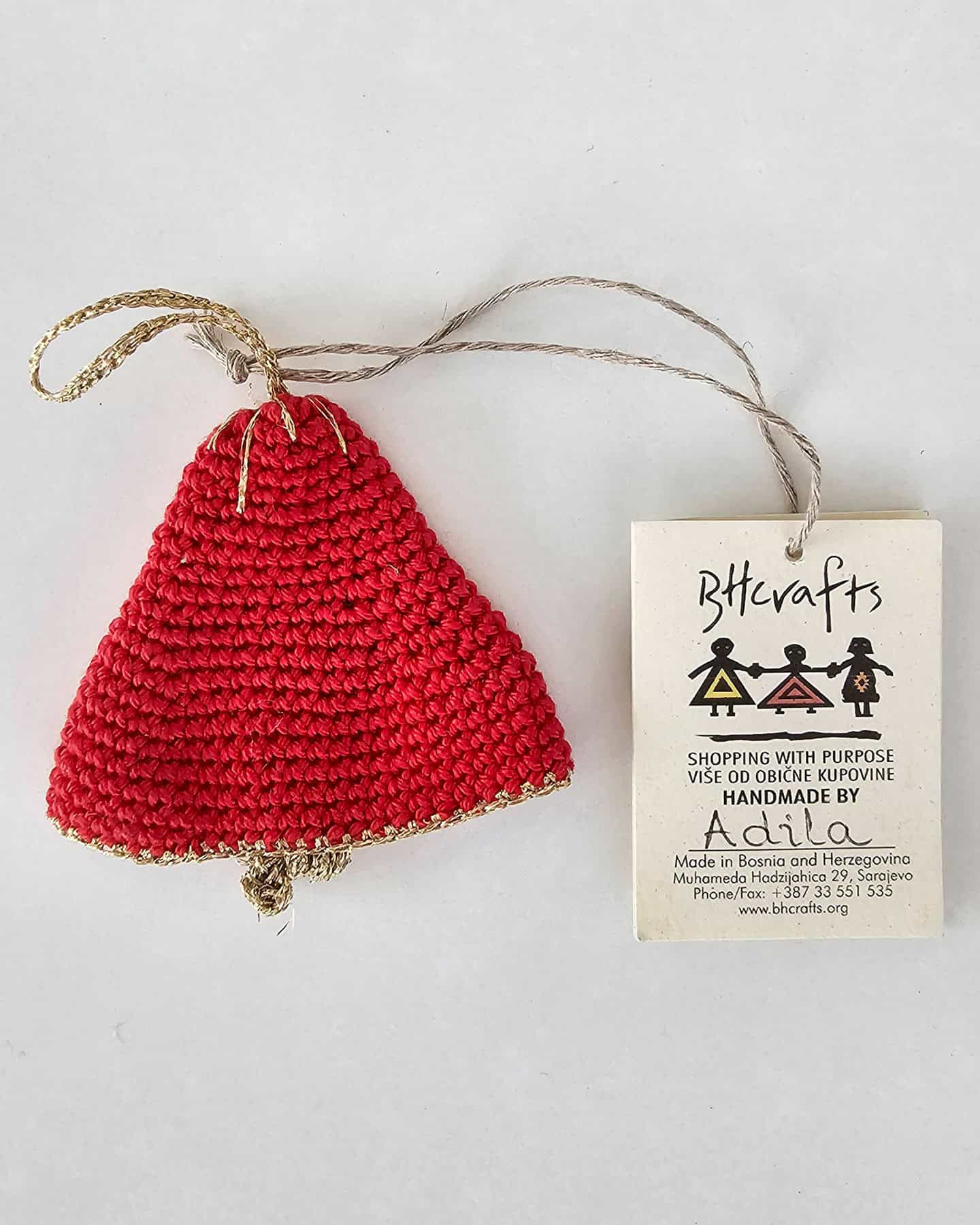 Red crocheted sachet jingle bell Christmas ornament with gold edging and loop, next to BHcrafts label handwritten by artisan Adila in Sarajevo. Perfect holiday decor