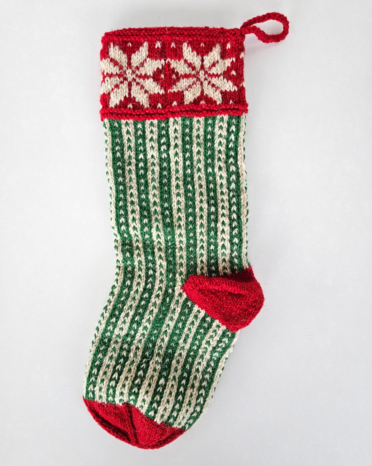 Hand-knit Christmas stocking with green and white stripes and red snowflake cuff