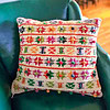 Hand-knitted pillow cover with colorful flower motifs and pom-poms