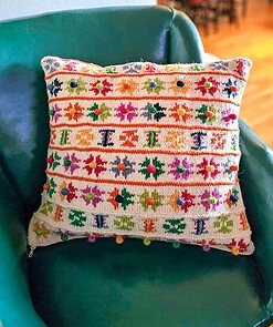 Hand-knitted pillow cover with colorful flower motifs and pom-poms