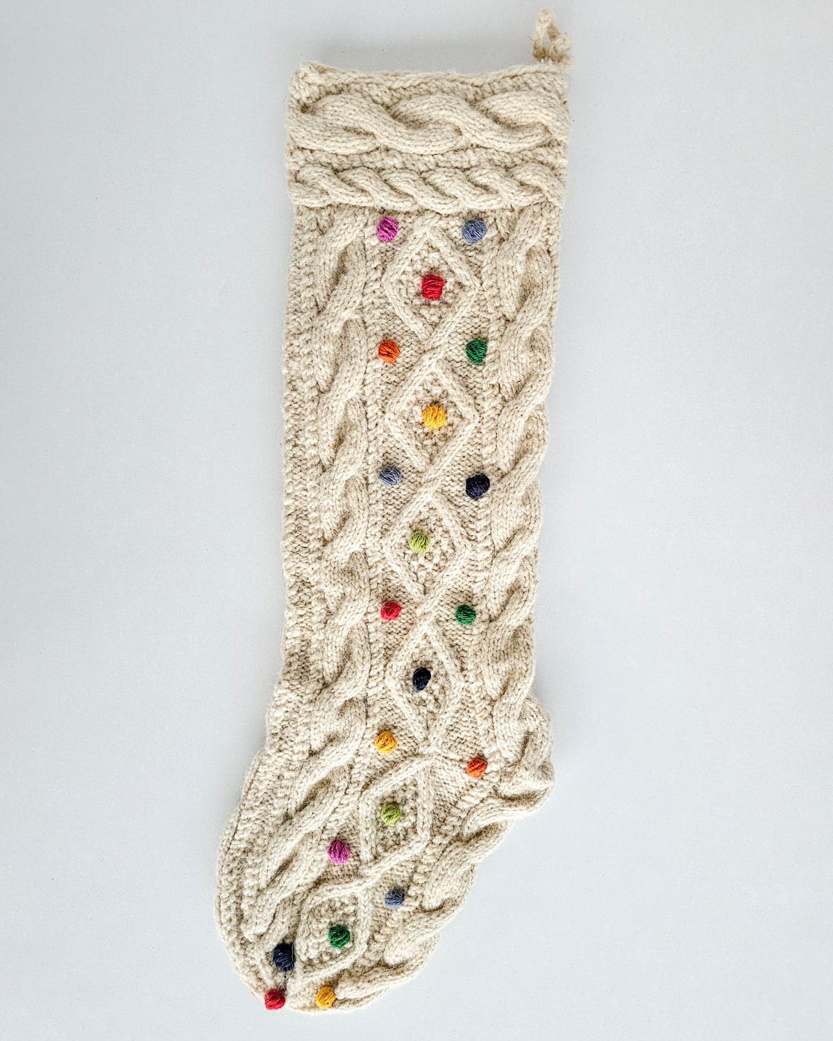 White hand-knit Christmas stockings with colorful dotted patterns and pom-poms