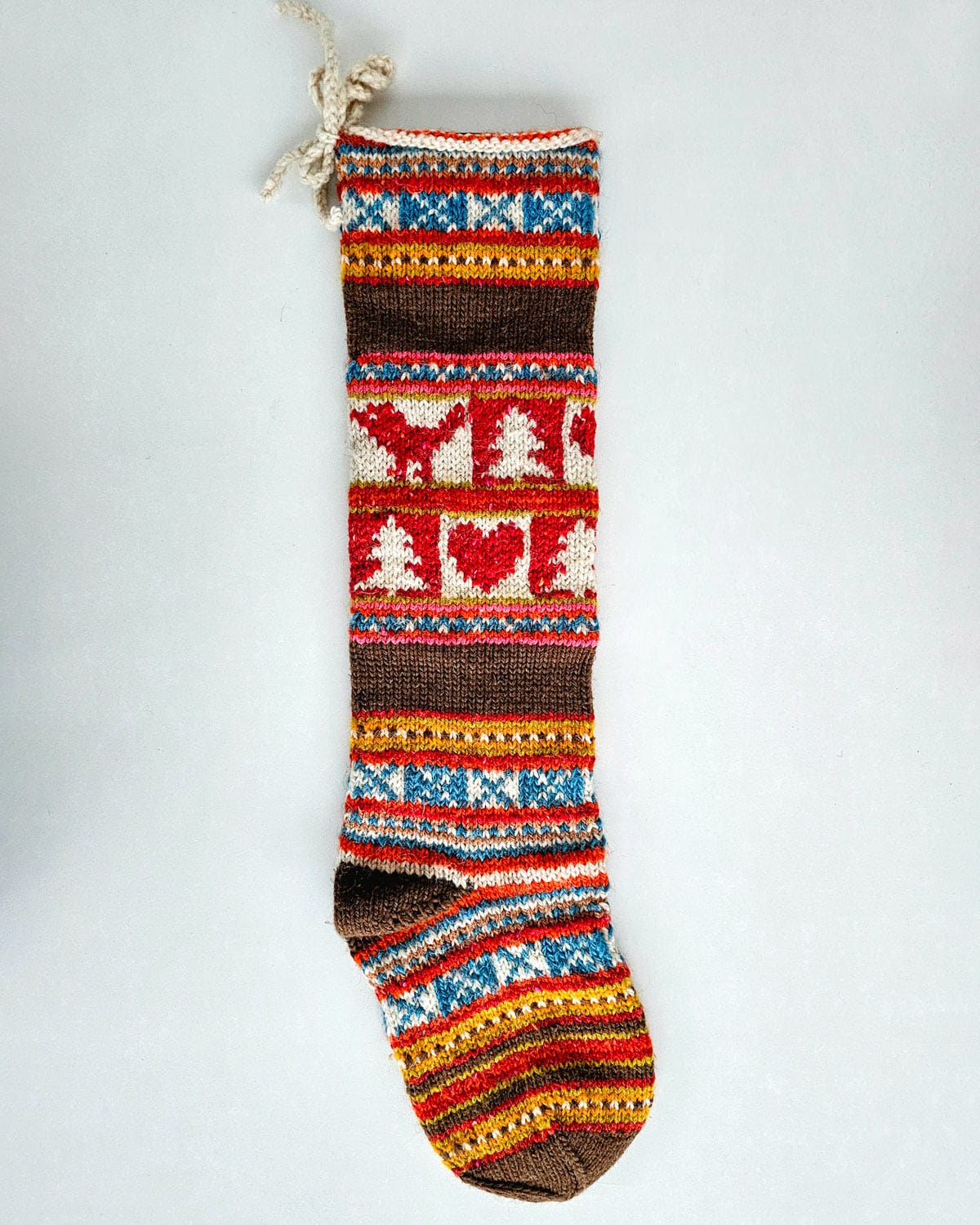 Artisan-made fair-trade knitted Christmas stocking with chevron stripes, hearts, and trees in brown, red, white, blue, and yellow.