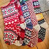 Bundle of five handmade snowflake Christmas stockings in red, white, blue, green, and yellow beside a jute tote bag.
