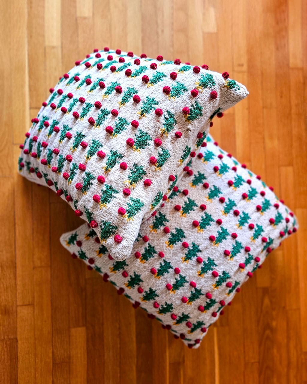Hand-knitted Christmas pillow cover with green trees and red pom-poms made by women artisans