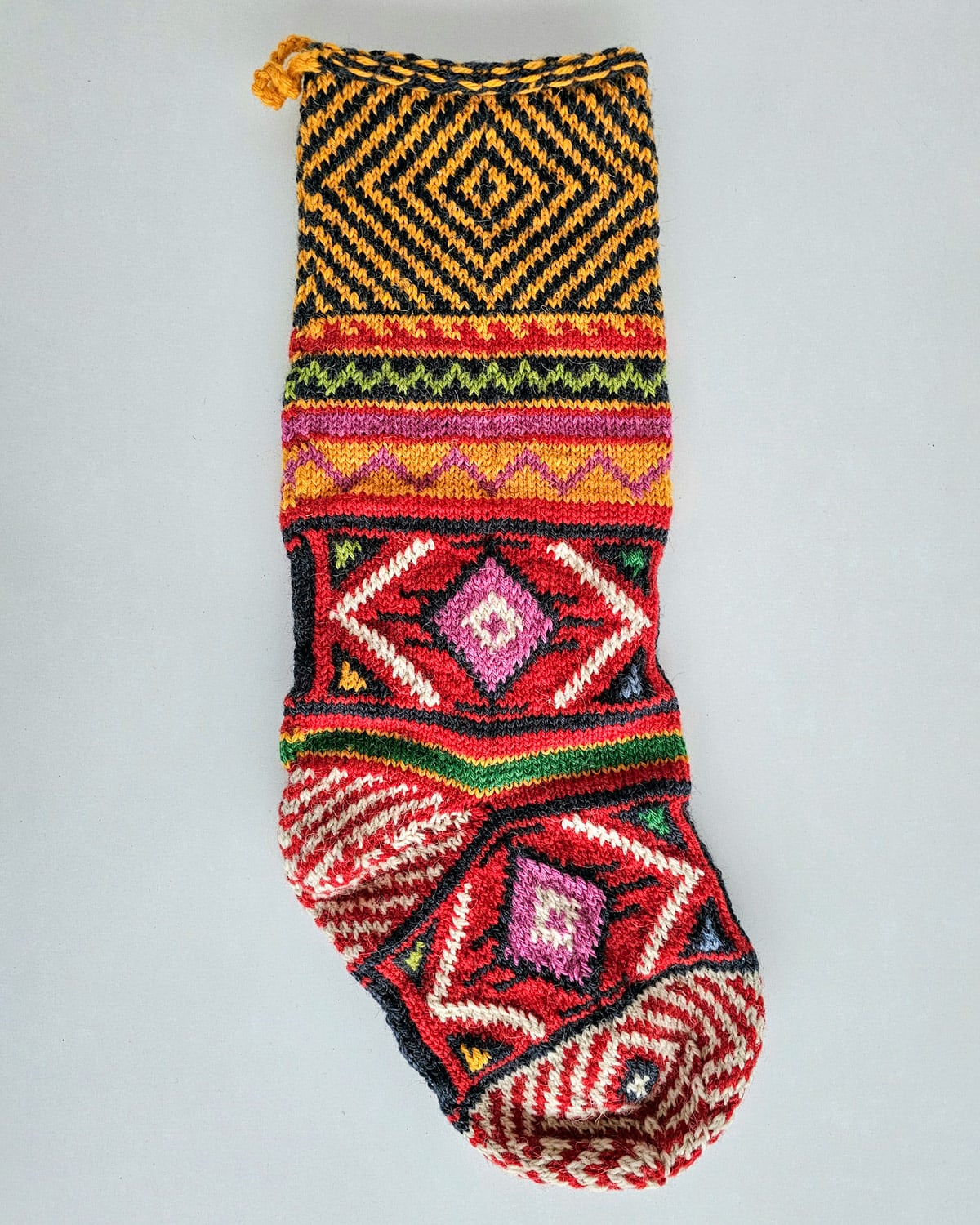 Hand-knit holiday stocking with bold geometric patterns in red, pink, green, yellow, and black