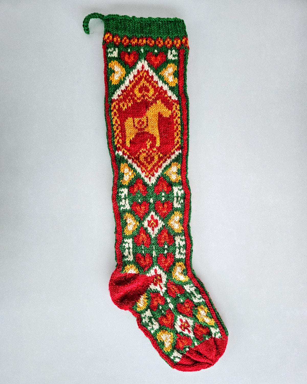 fair-trade Hand-knitted Christmas stocking in red, green, and yellow with heart and horse patterns.
