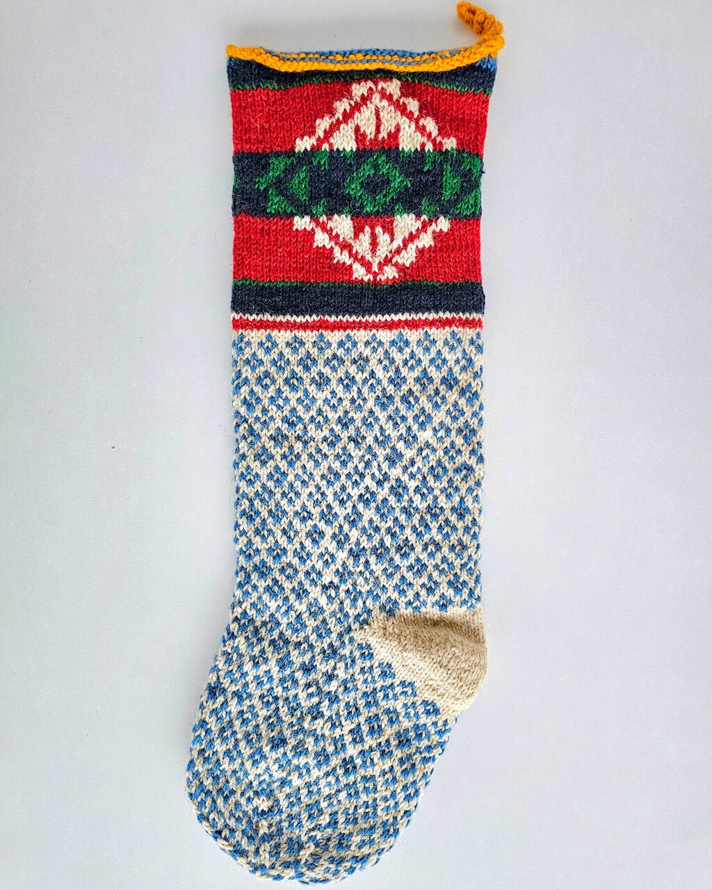 Hand-knitted BHcrafts Christmas stocking with traditional Bosnian folk pattern, featuring a blue and cream diamond body and a multi-colored geometric cuff.