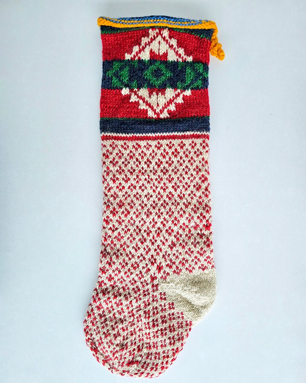 Hand-knitted BHcrafts Christmas stocking with traditional Bosnian red and cream geometric colorwork and multi-colored folk pattern cuff.