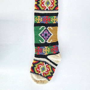 Handmade crochet Christmas stocking featuring bold tapestry-style geometric and floral patterns in vibrant colors.