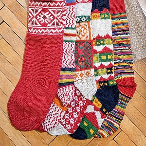 Five red themed knitted Christmas stockings with various patterns.