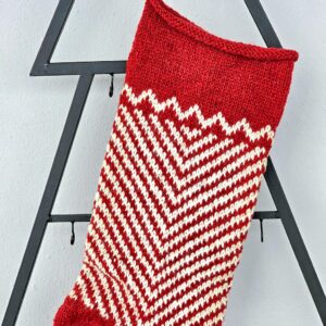 Top close up of Hand-knitted Christmas stocking with red and white chevron pattern hanging on blue cabinet.