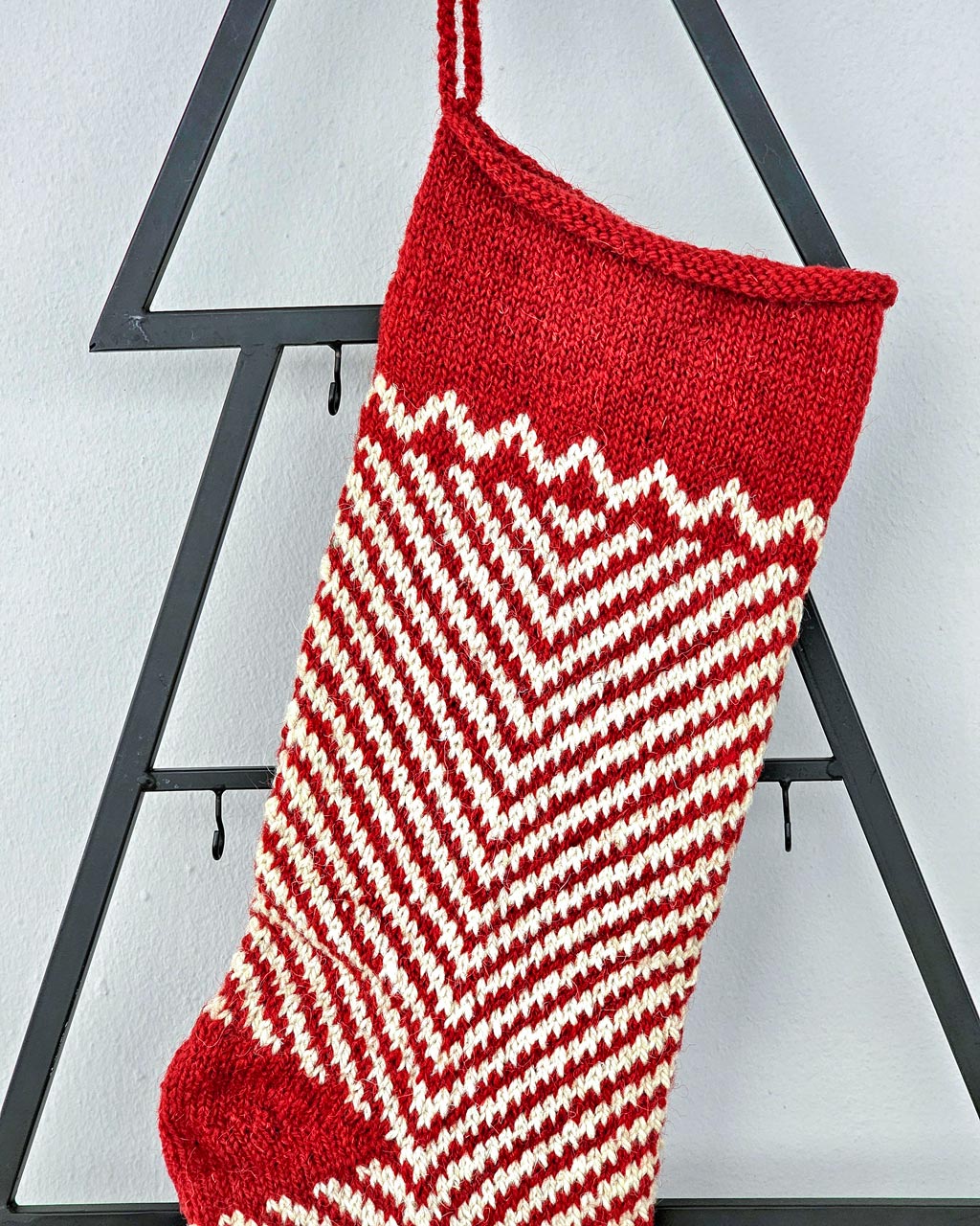 Top close up of Hand-knitted Christmas stocking with red and white chevron pattern hanging on blue cabinet.
