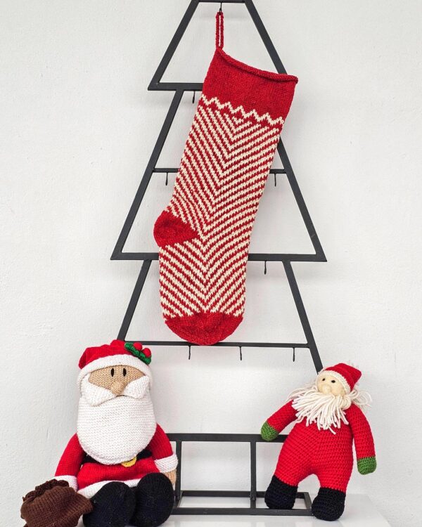 Hand-knitted Christmas stocking with red and white chevron pattern hanging on blue cabinet.