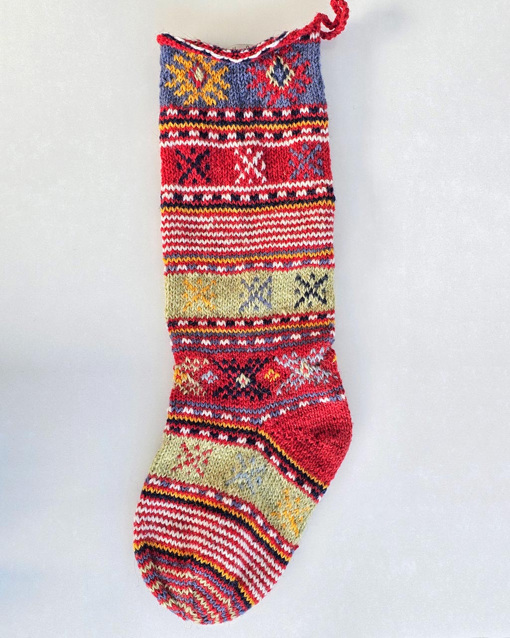 Red hand-knitted Christmas stocking with colourful folk patterns and a blue cuff