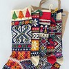 Five colorful handmade Christmas stockings on sale with folk patterns displayed in front of a jute tote bag